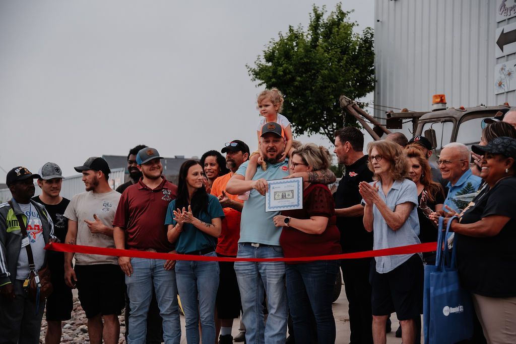 A group of people are standing around a red ribbon. | Chuck's Garage