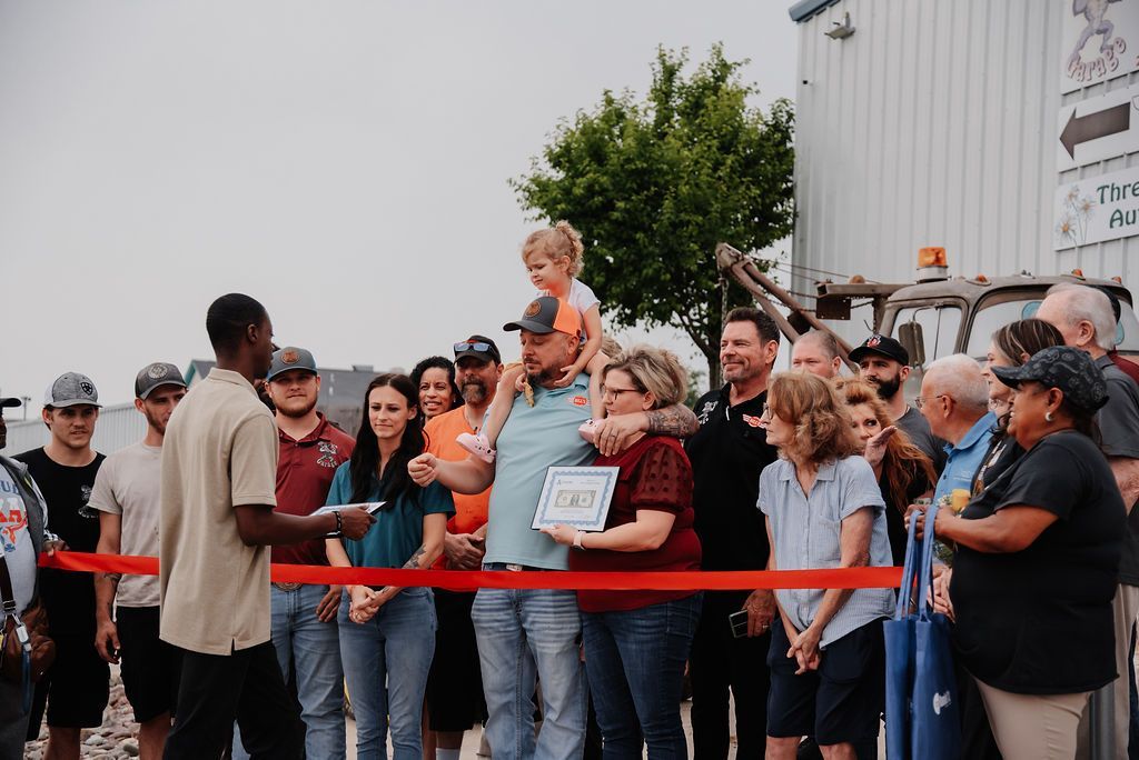 A man is cutting a red ribbon in front of a crowd of people. | Chuck's Garage