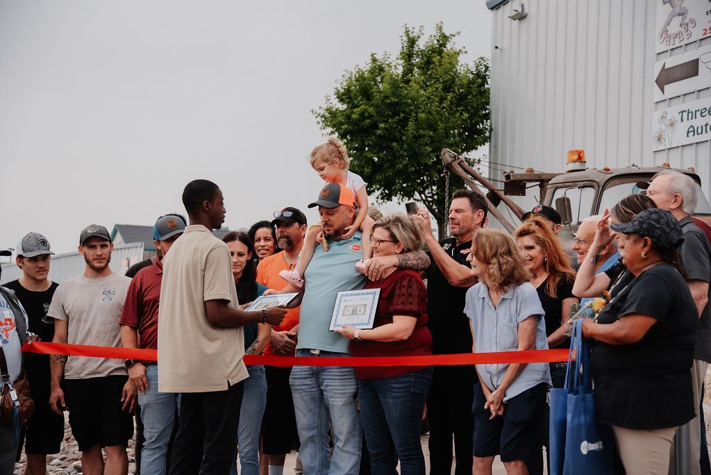A group of people are standing around a red ribbon. | Chuck's Garage