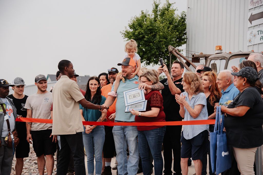 A group of people are standing around a ribbon cutting ceremony. | Chuck's Garage