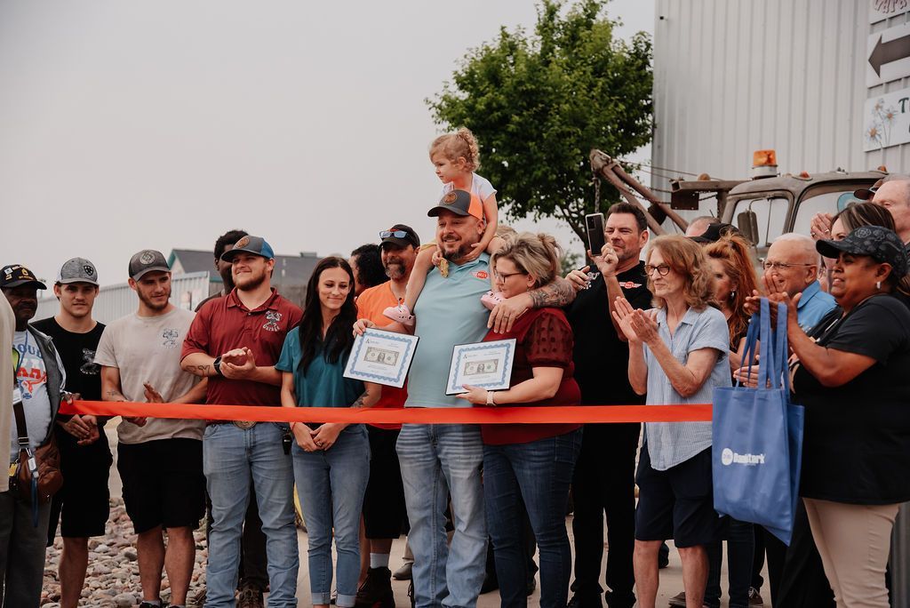 A group of people are standing around a red ribbon. | Chuck's Garage