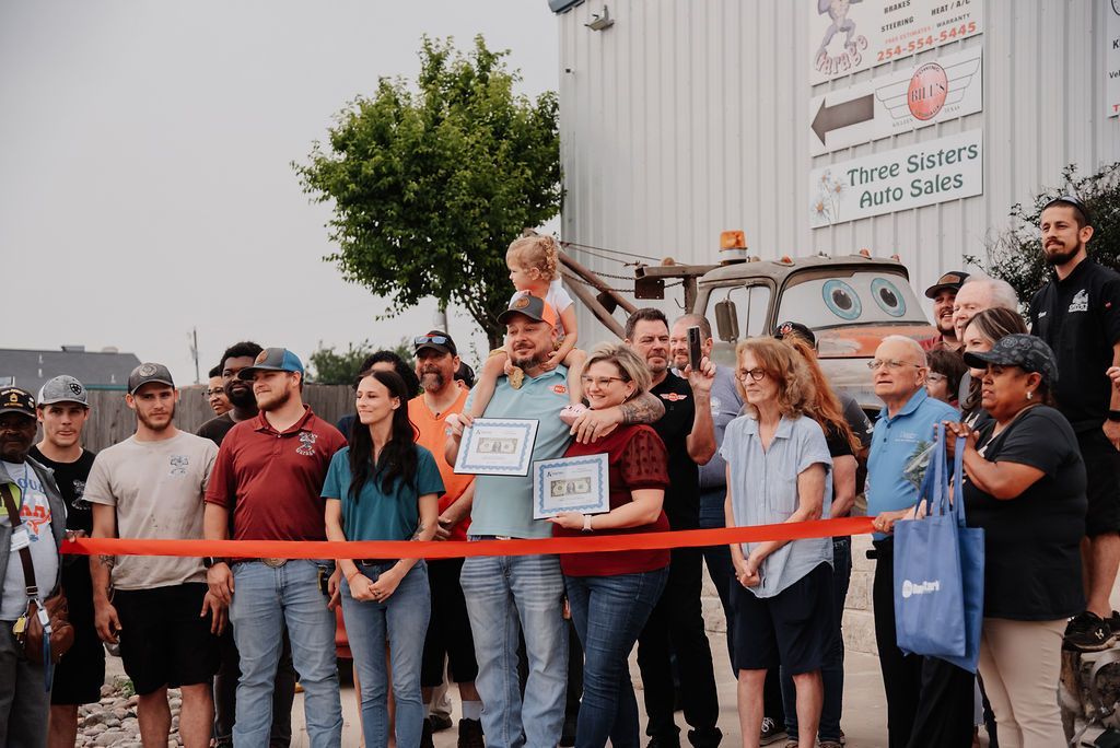 A group of people are standing in front of a building holding a red ribbon. | Chuck's Garage