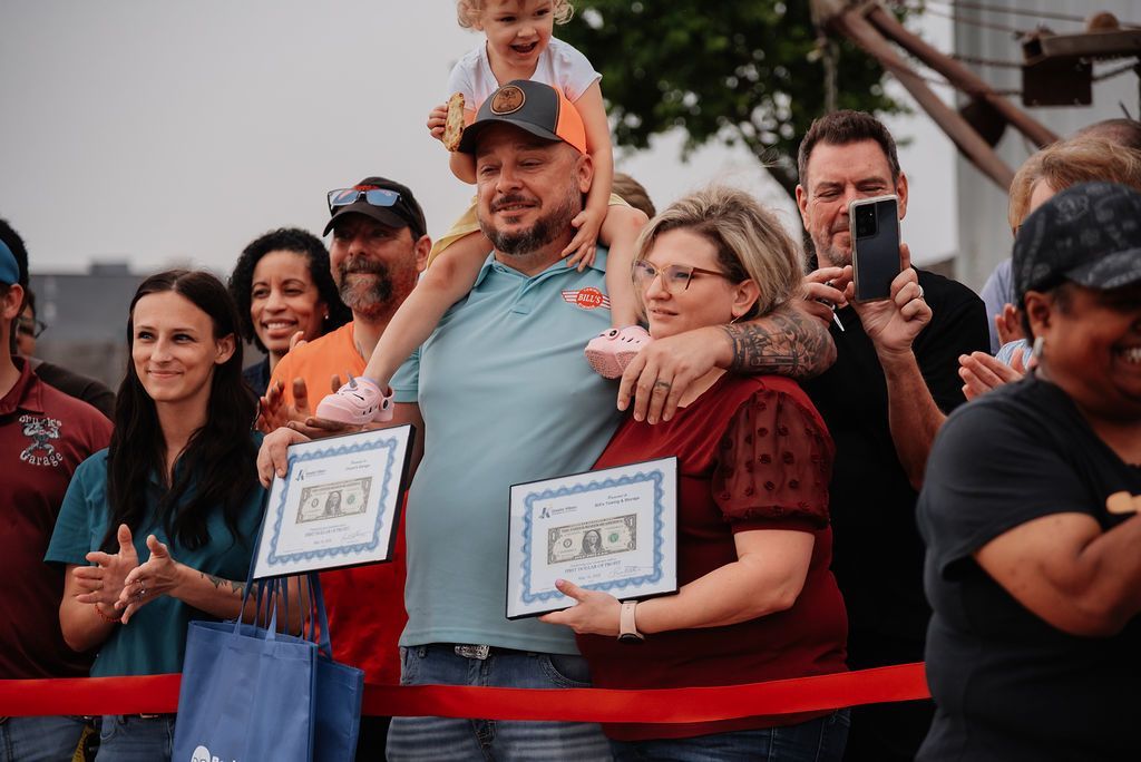 A group of people standing in front of a red ribbon holding certificates. | Chuck's Garage