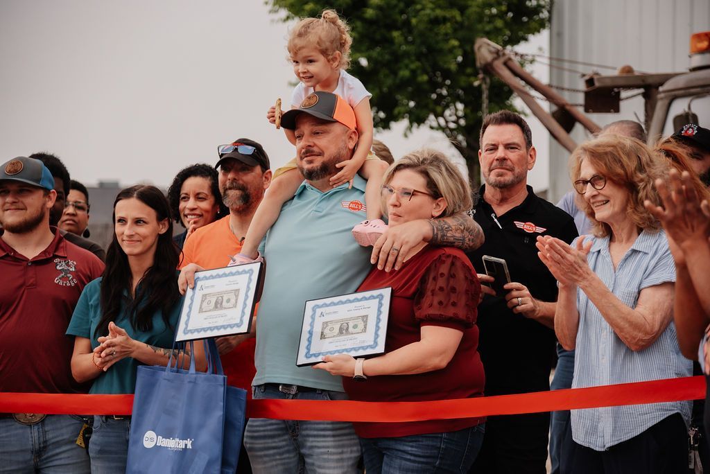A group of people are standing around a red ribbon. | Chuck's Garage