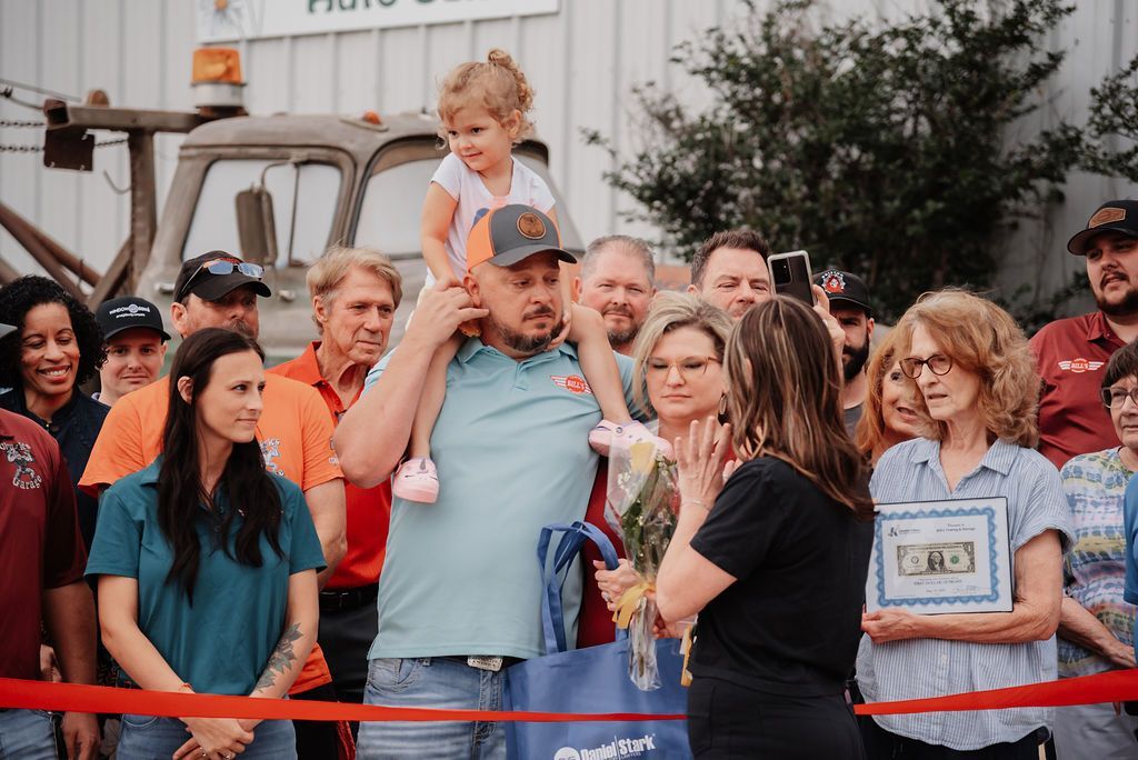 A man is carrying a little girl on his shoulders in front of a crowd of people. | Chuck's Garage
