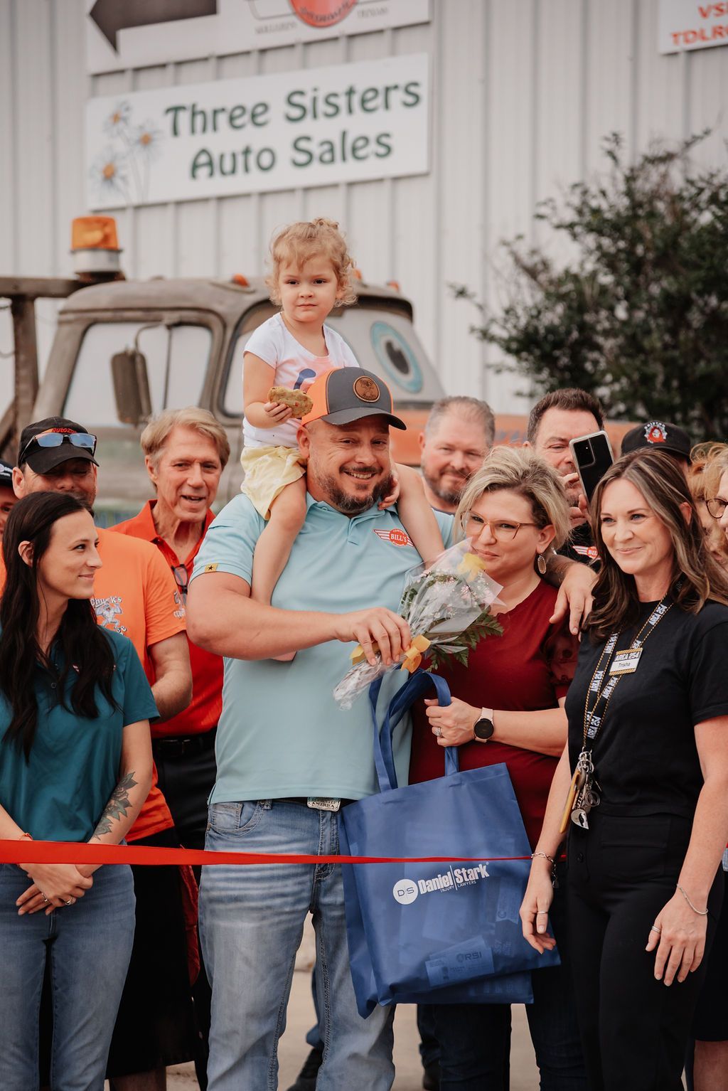 A man is holding a little girl on his shoulders at a ribbon cutting ceremony. | Chuck's Garage