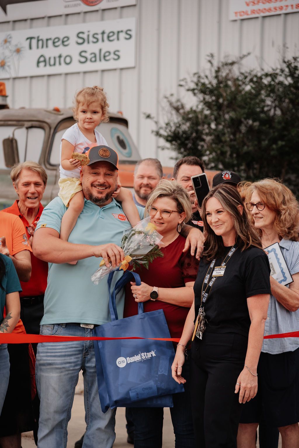 A man is holding a little girl on his shoulders at a ribbon cutting ceremony. | Chuck's Garage