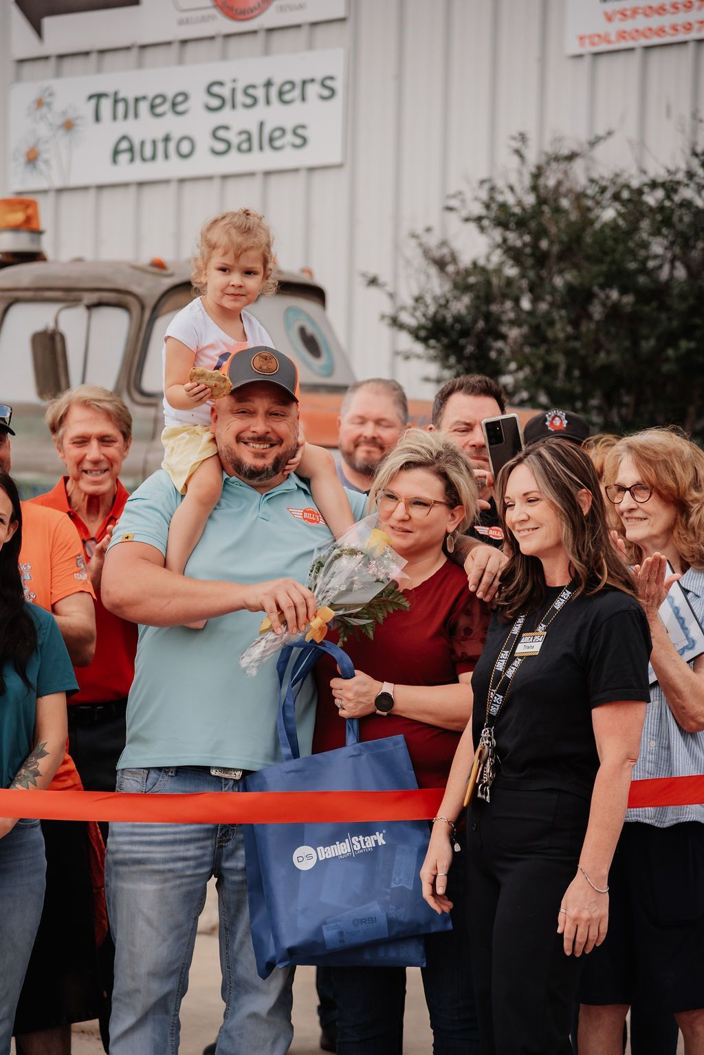 A man is holding a little girl on his shoulders at a ribbon cutting ceremony. | Chuck's Garage