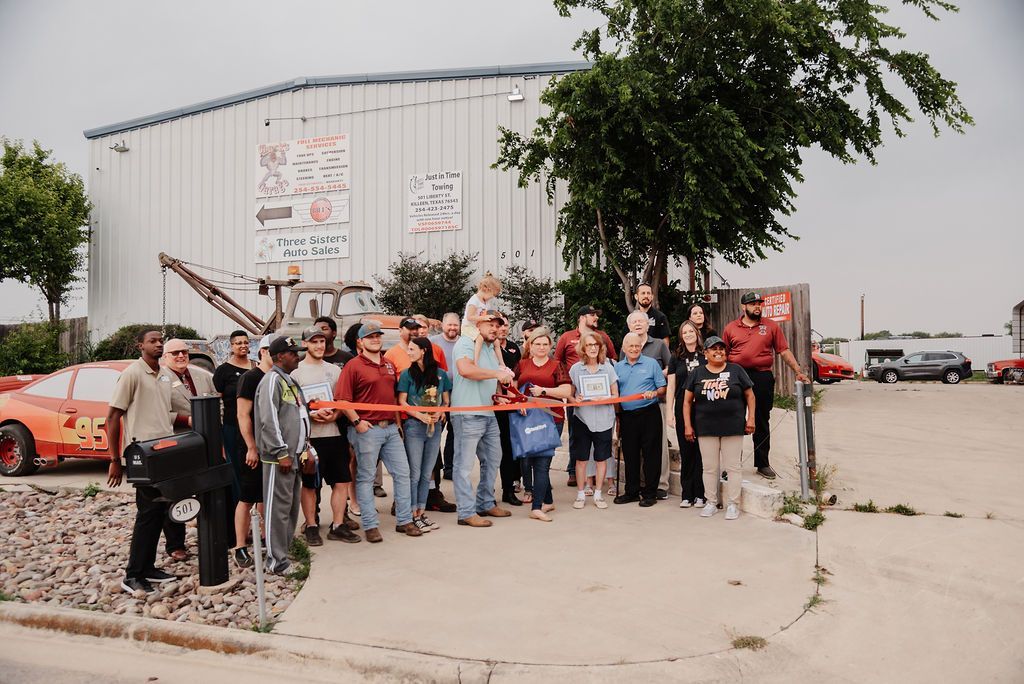 A group of people are standing in front of a building holding a red ribbon. | Chuck's Garage