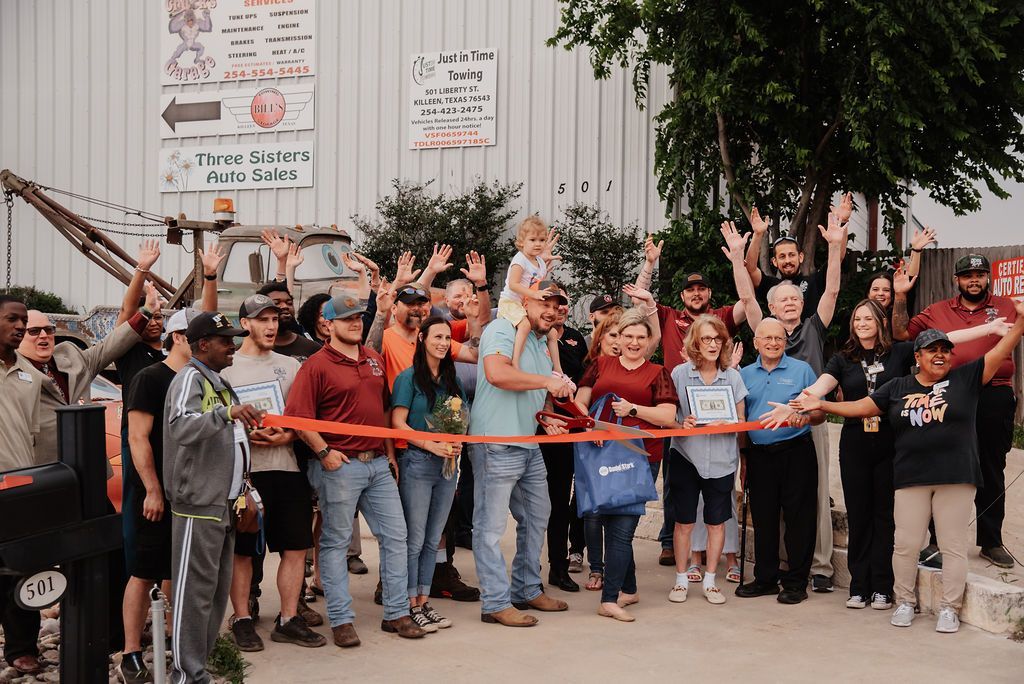 A large group of people are standing in front of a building holding a red ribbon. | Chuck's Garage