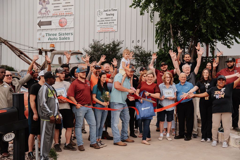 A large group of people are standing in front of a building cutting a red ribbon. | Chuck's Garage