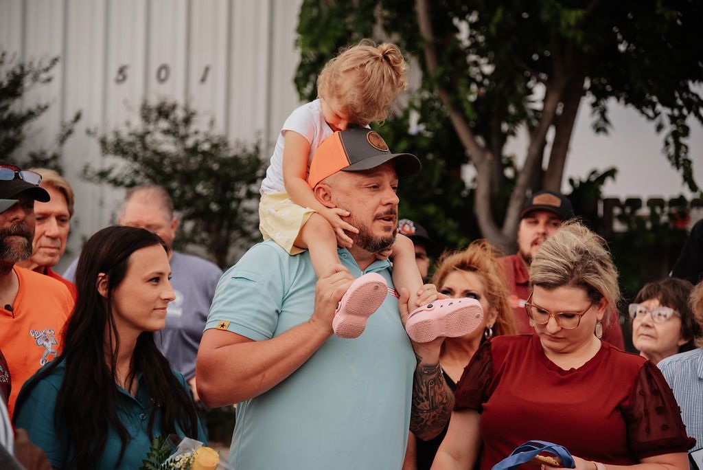 A man is carrying a little girl on his shoulders in front of a crowd of people. | Chuck's Garage