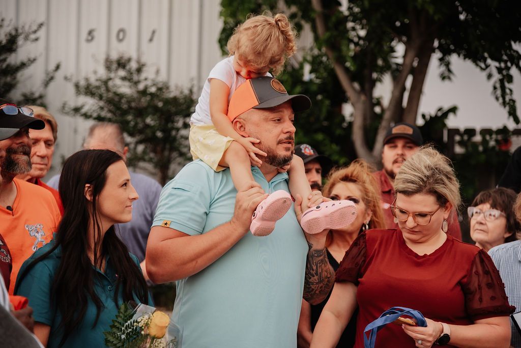 A man is carrying a little girl on his shoulders in front of a crowd of people. | Chuck's Garage