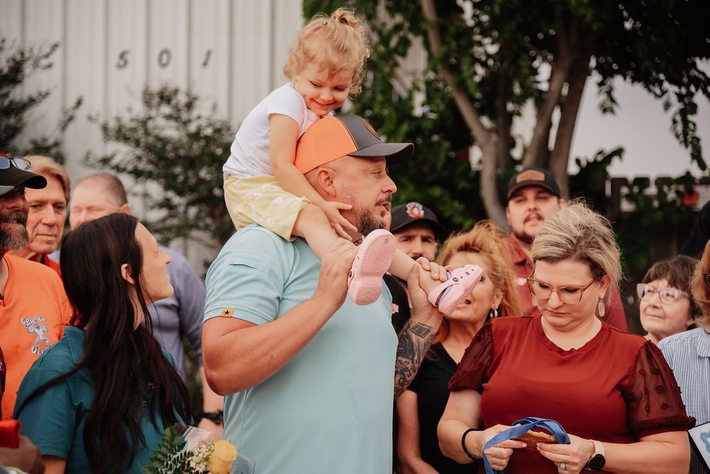 A man is carrying a little girl on his shoulders in front of a crowd of people. | Chuck's Garage