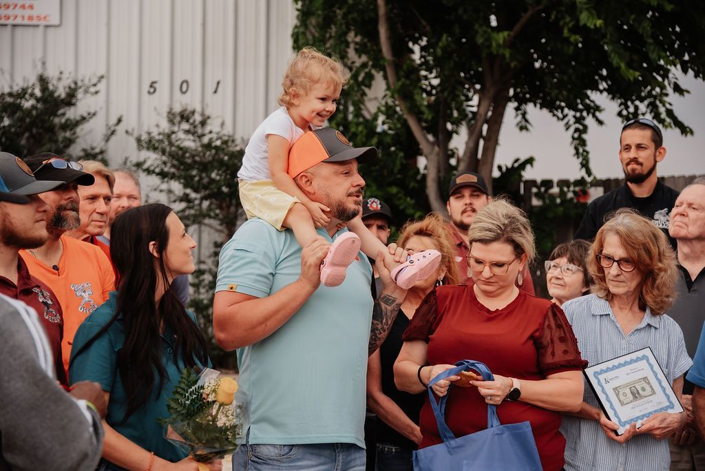 A man is carrying a baby on his shoulders in front of a crowd of people. | Chuck's Garage