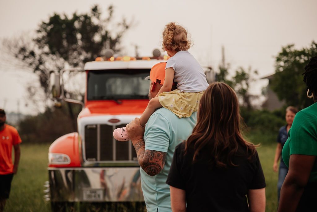 A man is carrying a little girl on his shoulders in front of a truck. | Chuck's Garage
