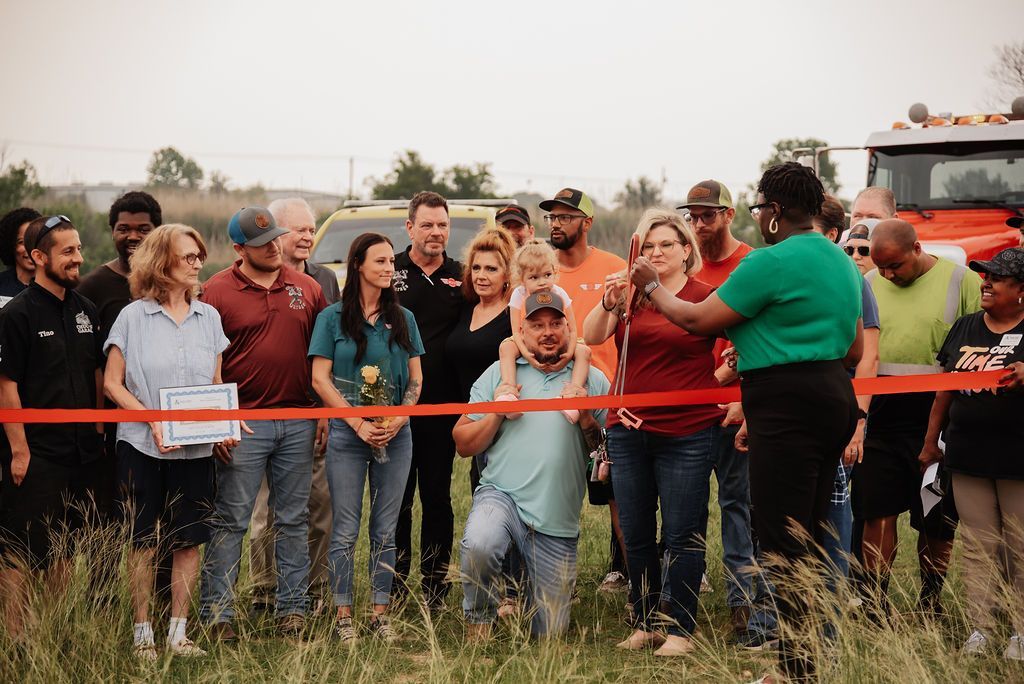 A group of people are standing in a field holding a red ribbon. | Chuck's Garage