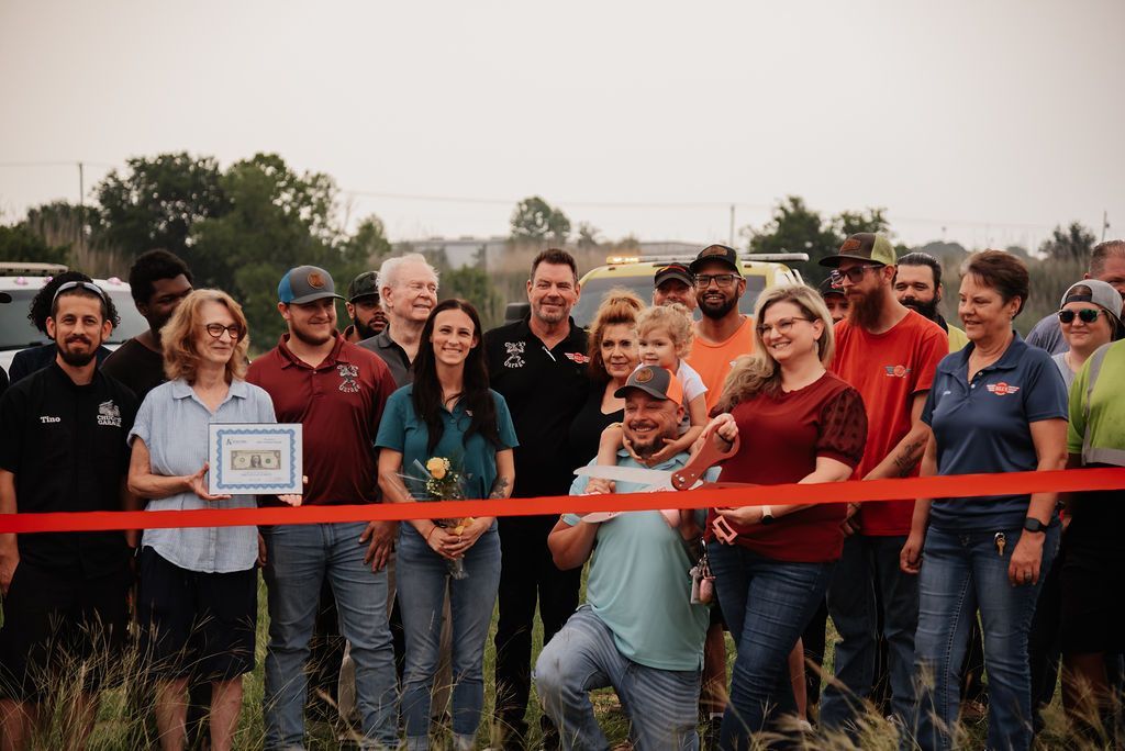 A group of people are standing in a field holding a red ribbon. | Chuck's Garage