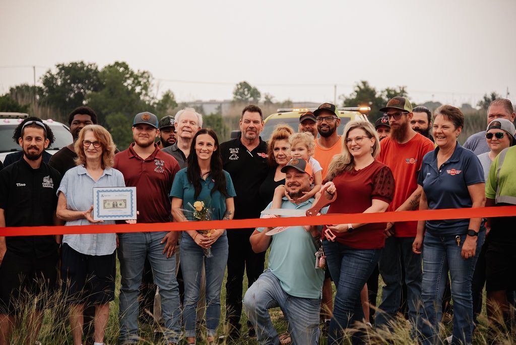A group of people are standing in front of a red ribbon. | Chuck's Garage