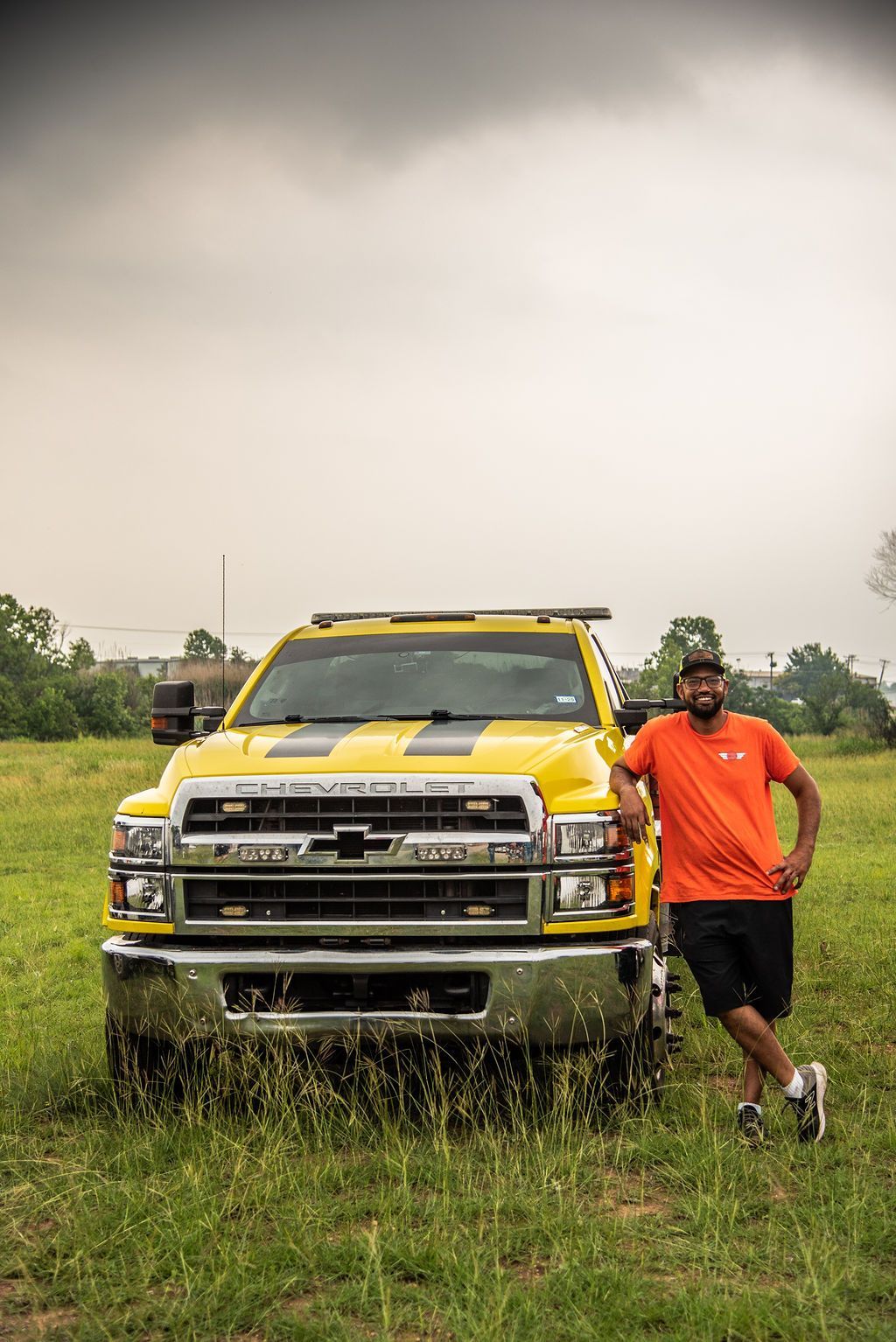 A man is standing in front of a yellow tow truck in a grassy field. | Chuck's Garage