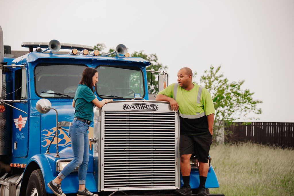 A man and a woman are standing next to a blue semi truck. | Chuck's Garage