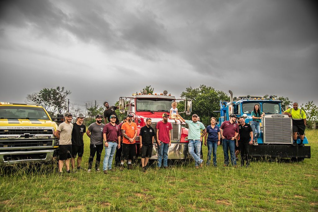 A group of people standing next to trucks in a field. | Chuck's Garage