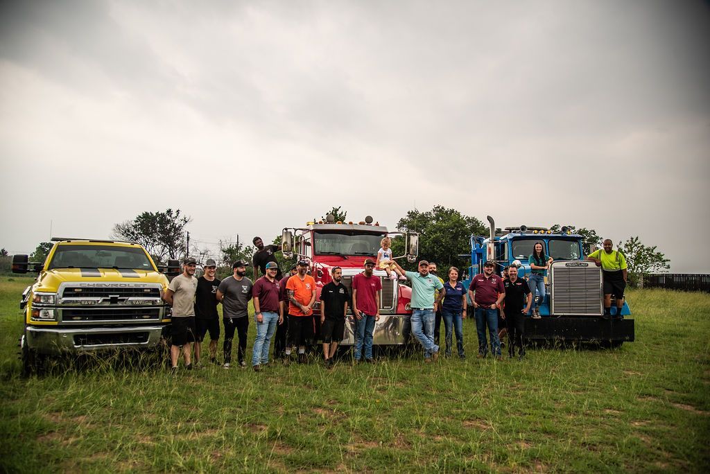 A group of people standing in front of trucks in a field. | Chuck's Garage