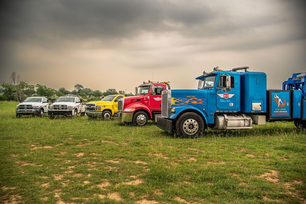 A row of tow trucks are parked in a grassy field. | Chuck's Garage