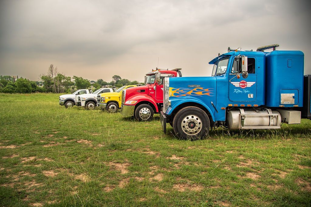 A row of semi trucks are parked in a grassy field. | Chuck's Garage