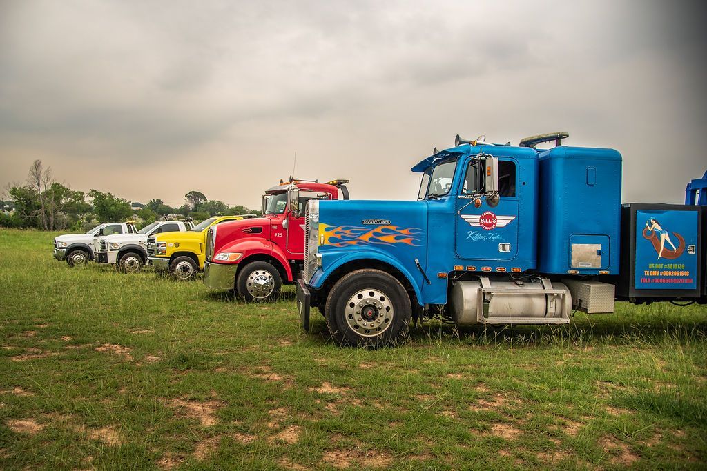 A row of tow trucks are parked in a grassy field. | Chuck's Garage