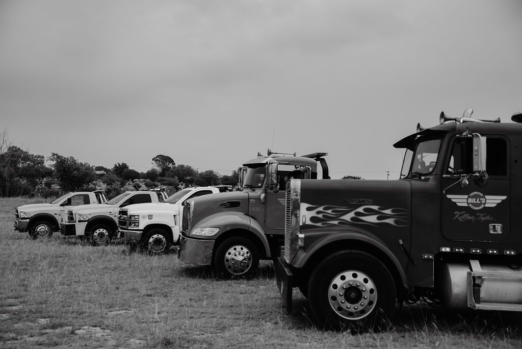 A black and white photo of a row of tow trucks parked in a field. | Chuck's Garage