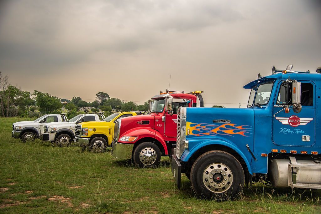 A row of tow trucks are parked in a grassy field. | Chuck's Garage
