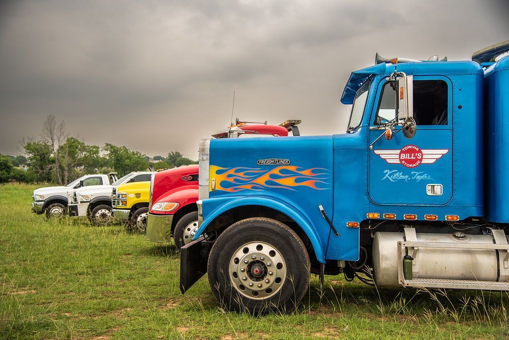 A row of semi trucks are parked in a grassy field. | Chuck's Garage