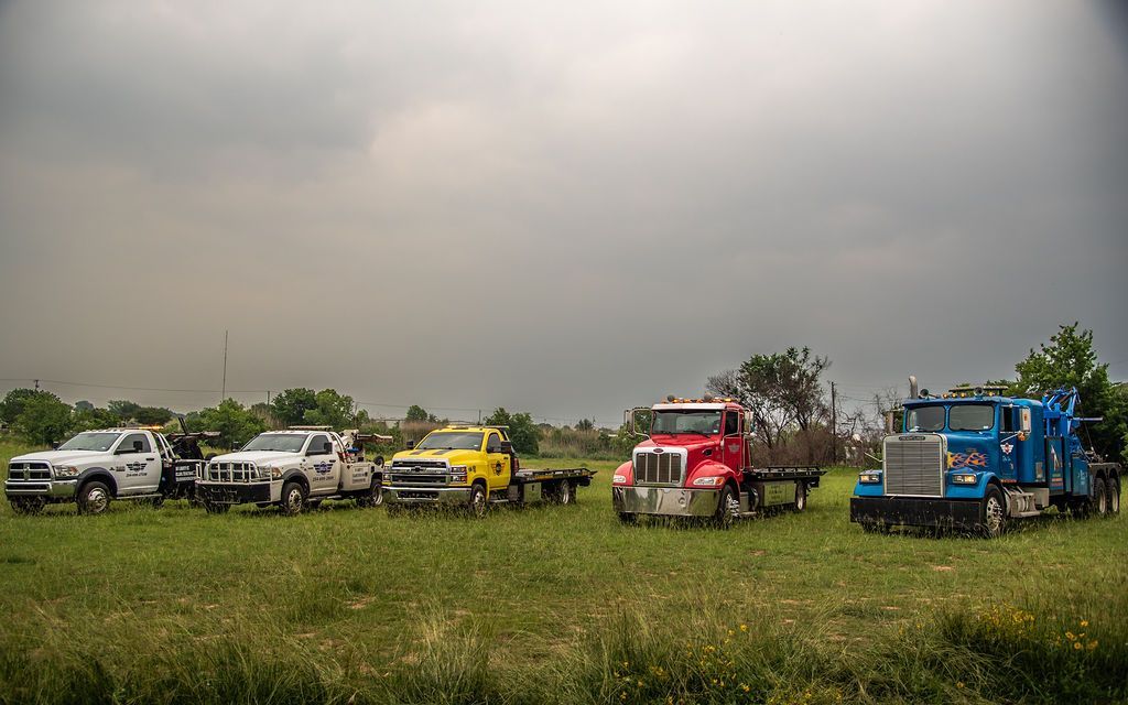 A row of tow trucks are parked in a grassy field. | Chuck's Garage