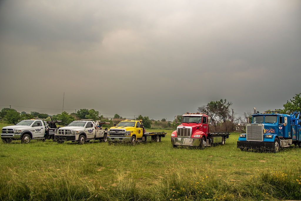 A row of tow trucks are parked in a grassy field. | Chuck's Garage