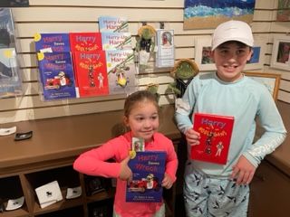 Two children holding "Harry Wreck" books, smiling at the camera in a store.