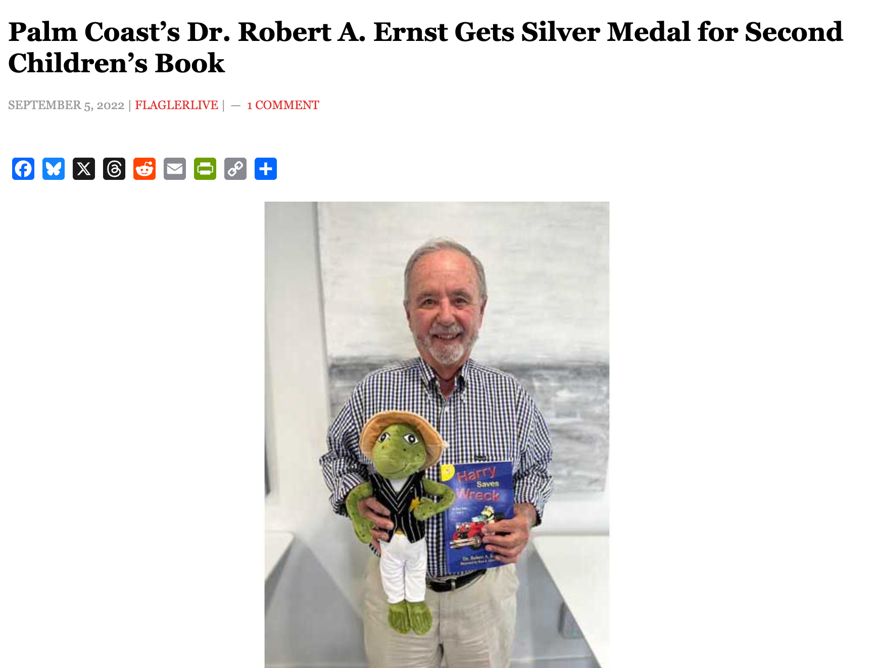 Dr. Robert A. Ernst holding a book and a frog toy. He’s in Palm Coast.