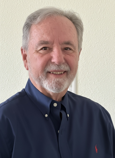 Older man with gray hair and beard, smiling. Wearing a blue button-down shirt.