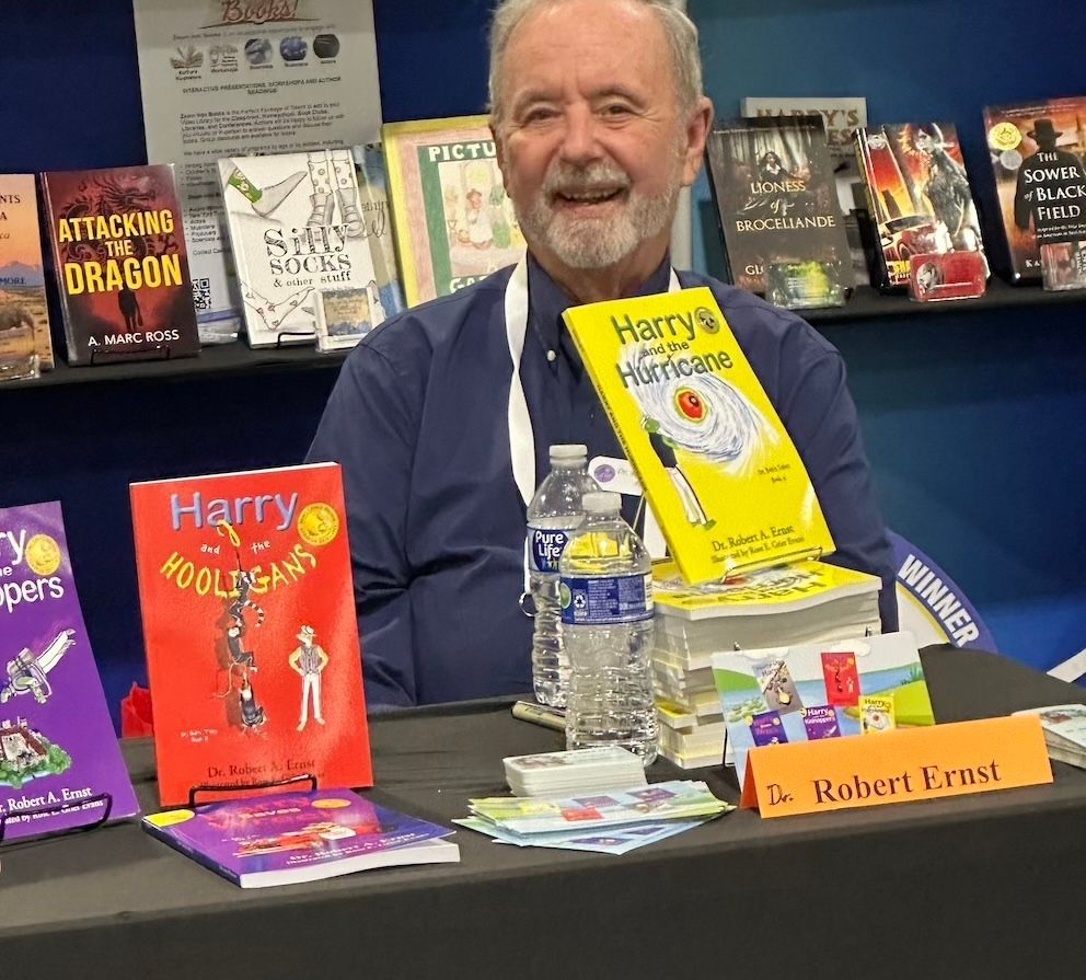 Author Robert Krouse smiling at a book table, holding his book