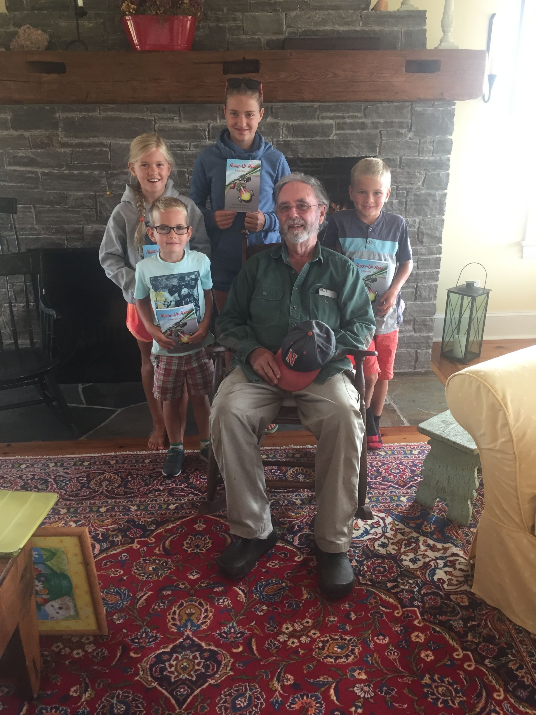 Man seated with four children in front of a stone fireplace; all are smiling.