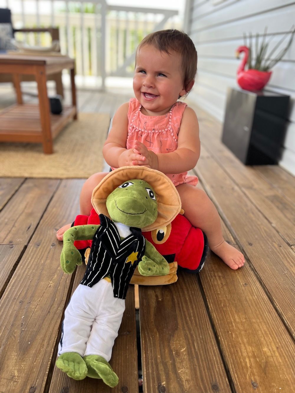Stuffed frog wearing a hat, vest, and white pants, striking a pose.