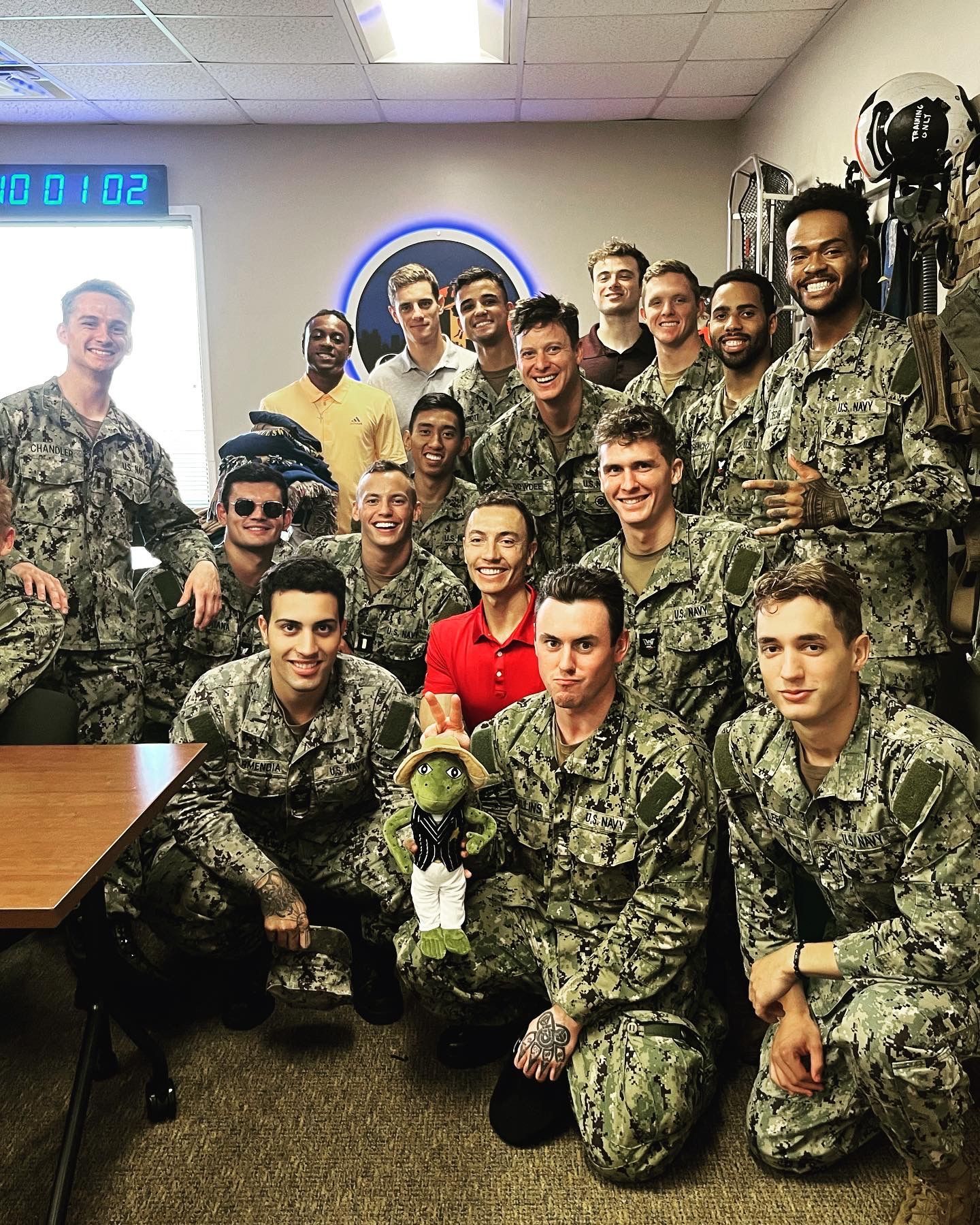 Group of Navy personnel in camouflage uniforms, smiling, posing together in a room.