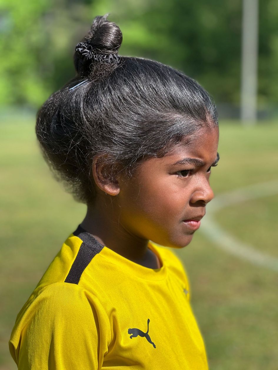 Football players in action on a grassy field; one runs with the ball, pursued by two opponents.
