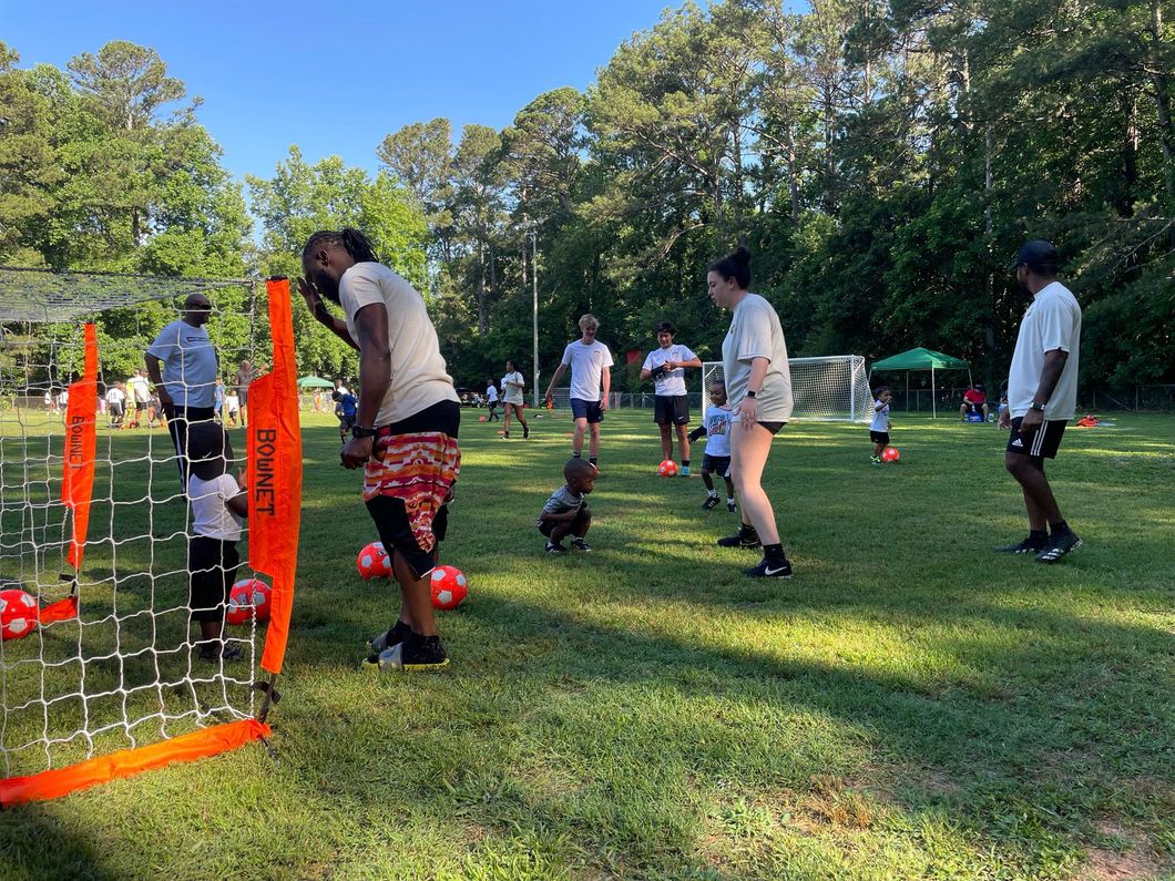 Flag football game at night, a player in red jersey runs with the ball as others pursue on a green field.
