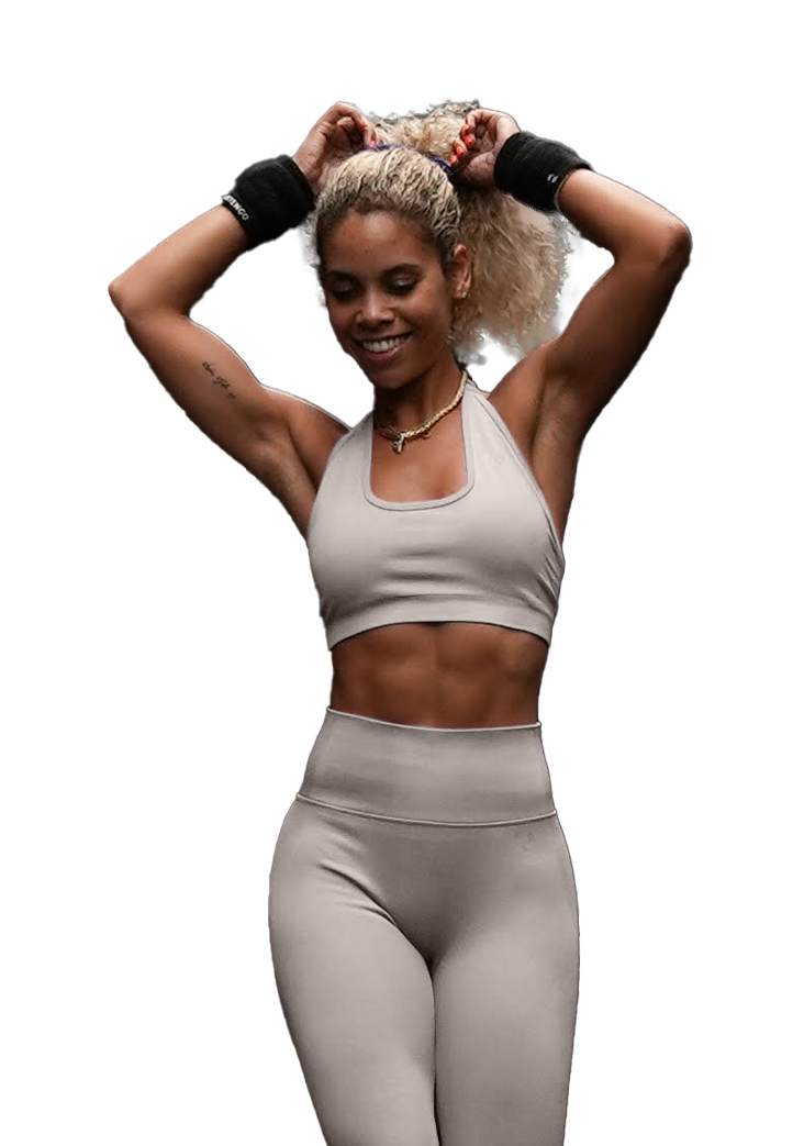 A woman in a pink sports bra and leggings is standing with her hands in her hair.