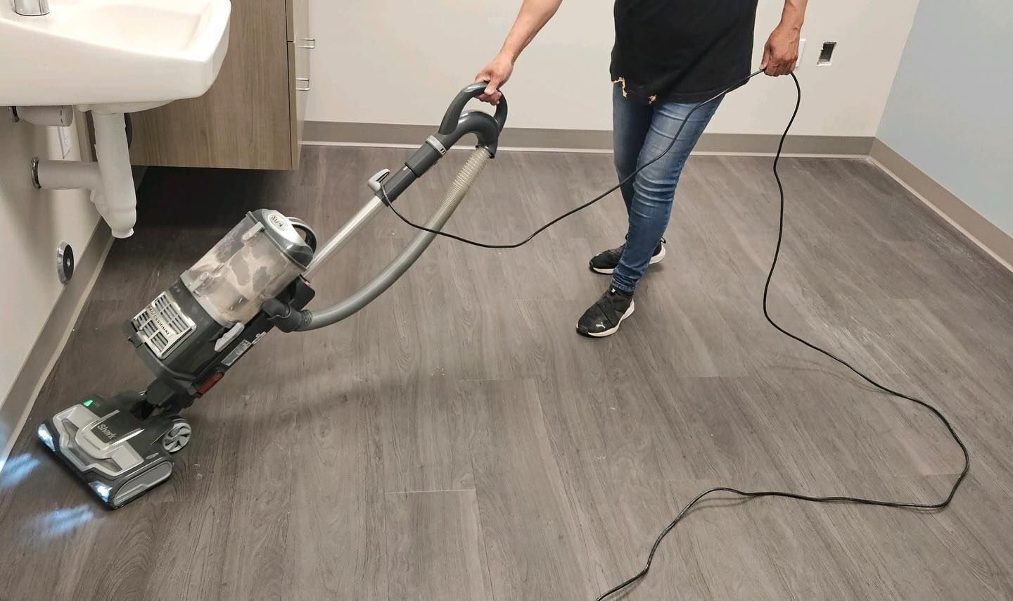 A person is using a vacuum cleaner on a wooden floor.