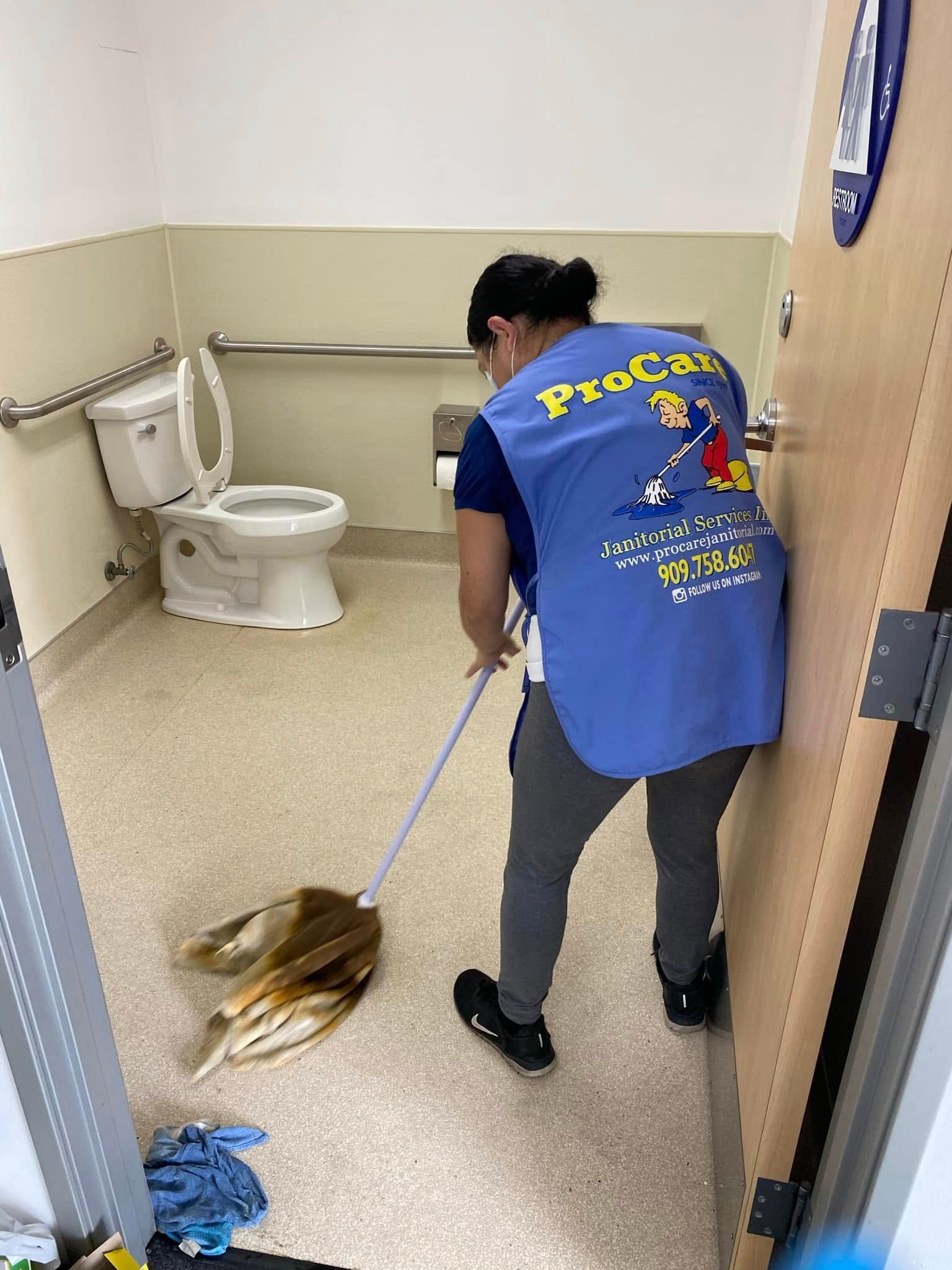 A woman is cleaning a bathroom floor with a mop.