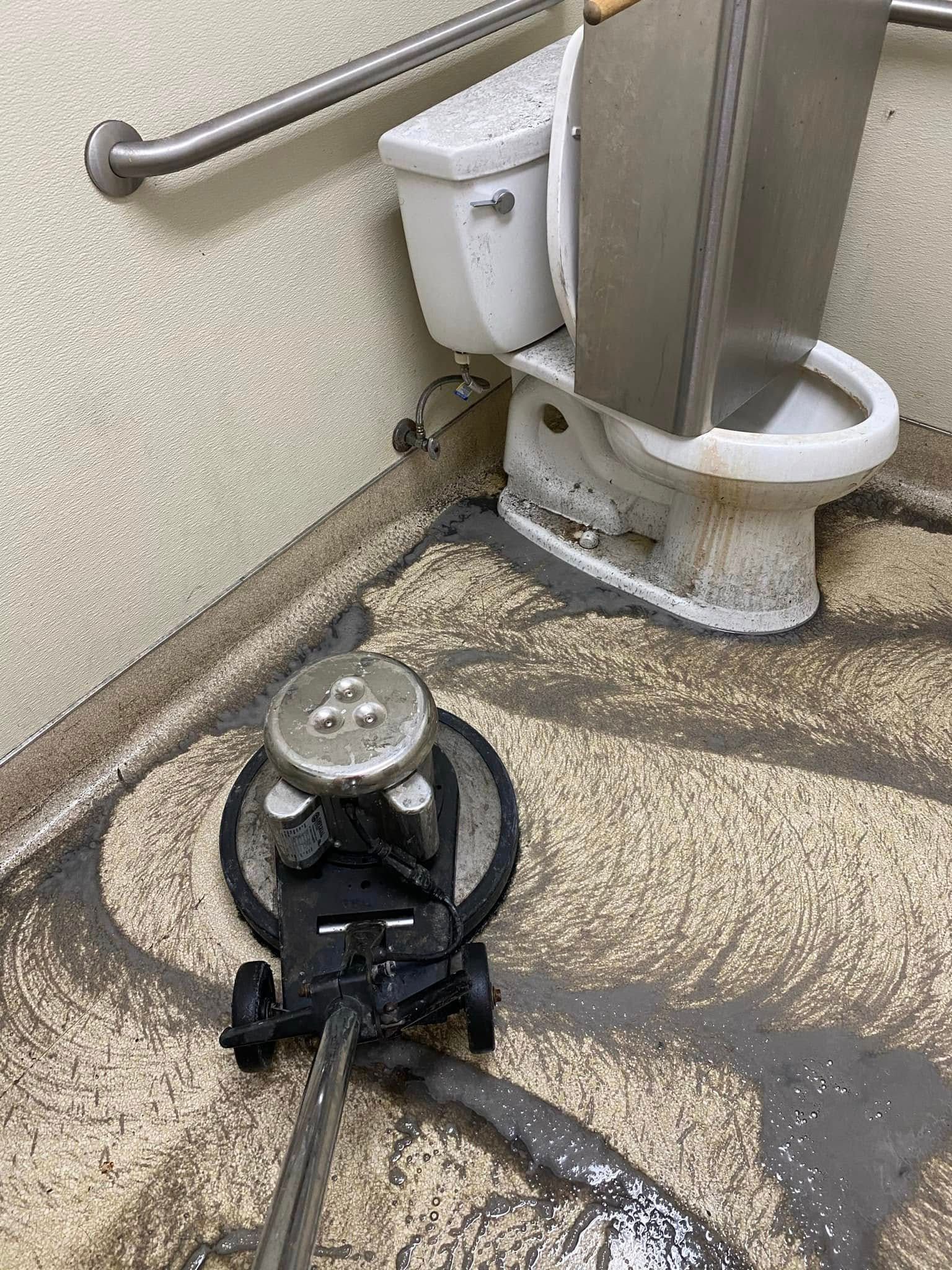 A toilet is sitting in a bathroom next to a vacuum cleaner.