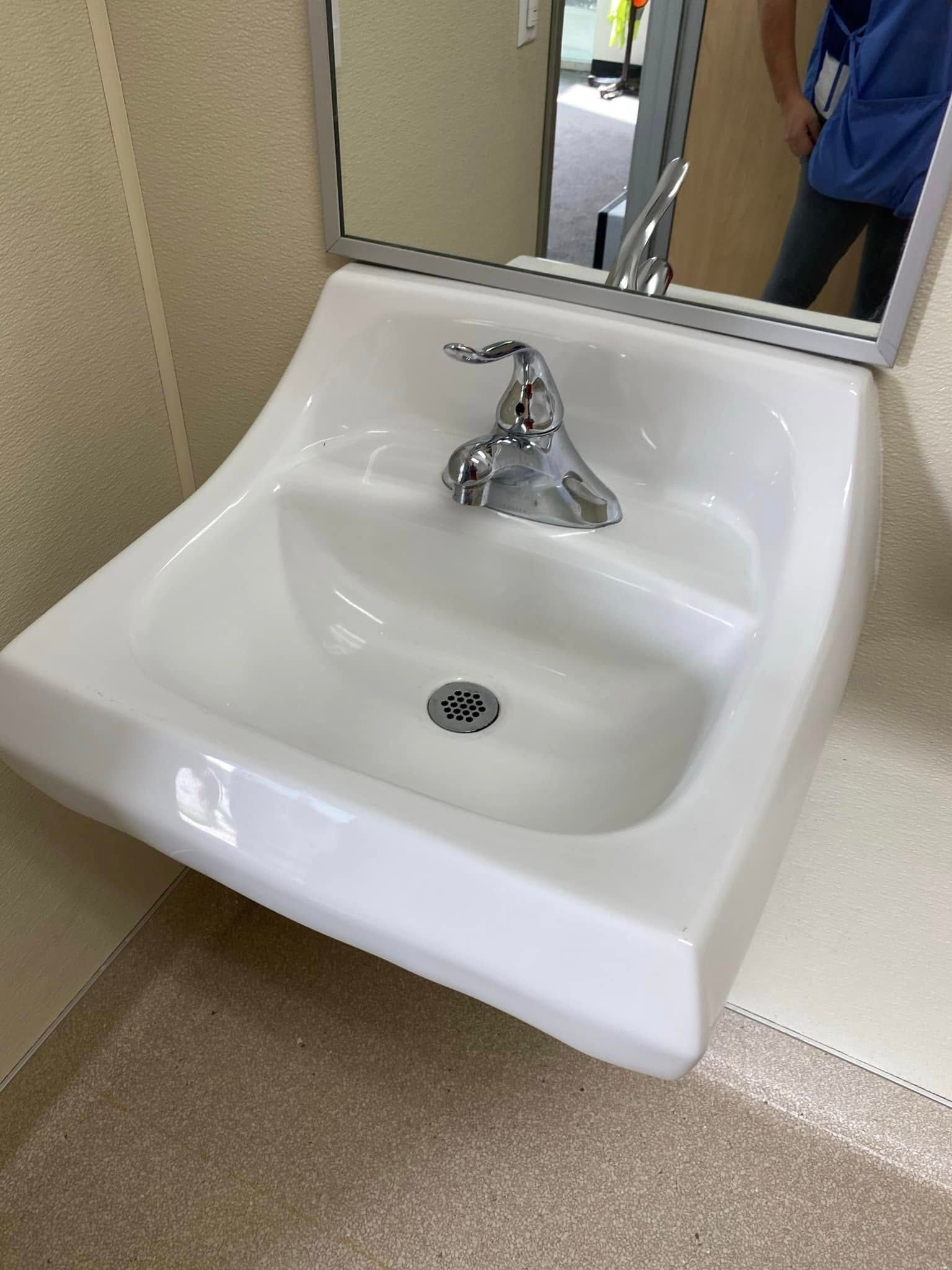 A bathroom sink with a mirror above it and a person standing in the mirror.