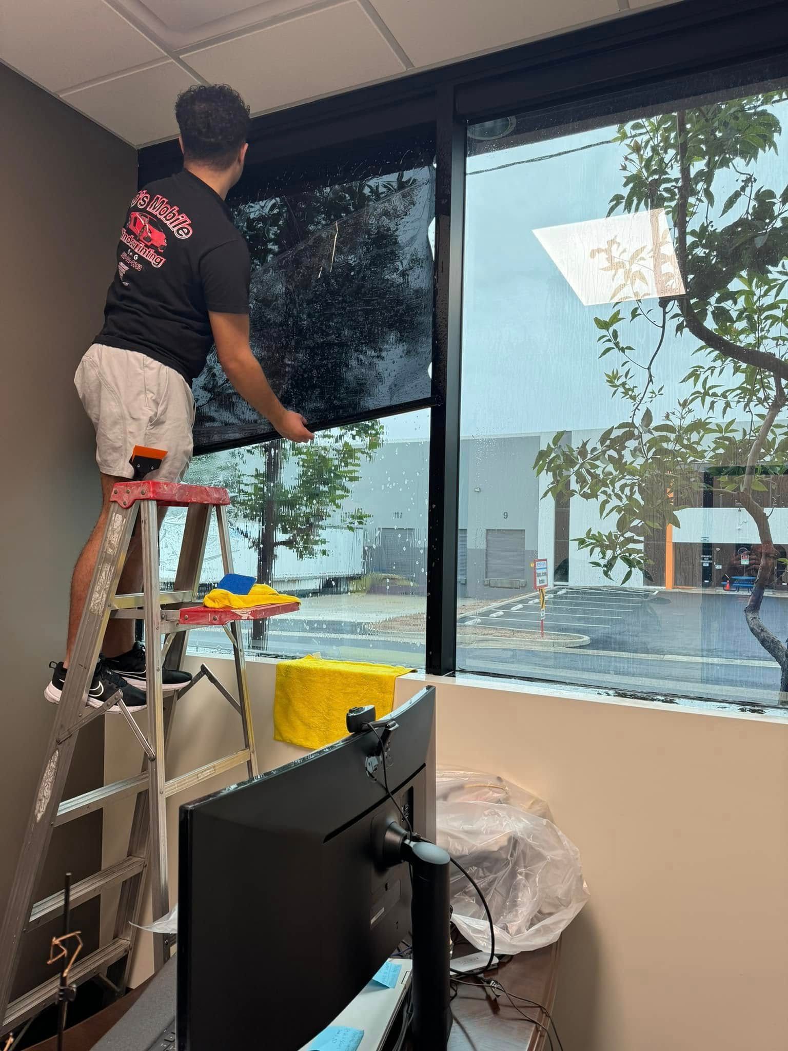 A man is standing on a ladder cleaning a window.